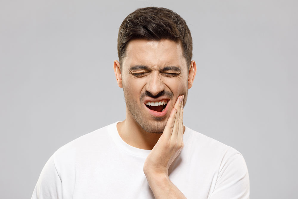 Young guy with closed eyes suffering from severe toothache, touching jaw with fingers trying to ease strong tooth pain