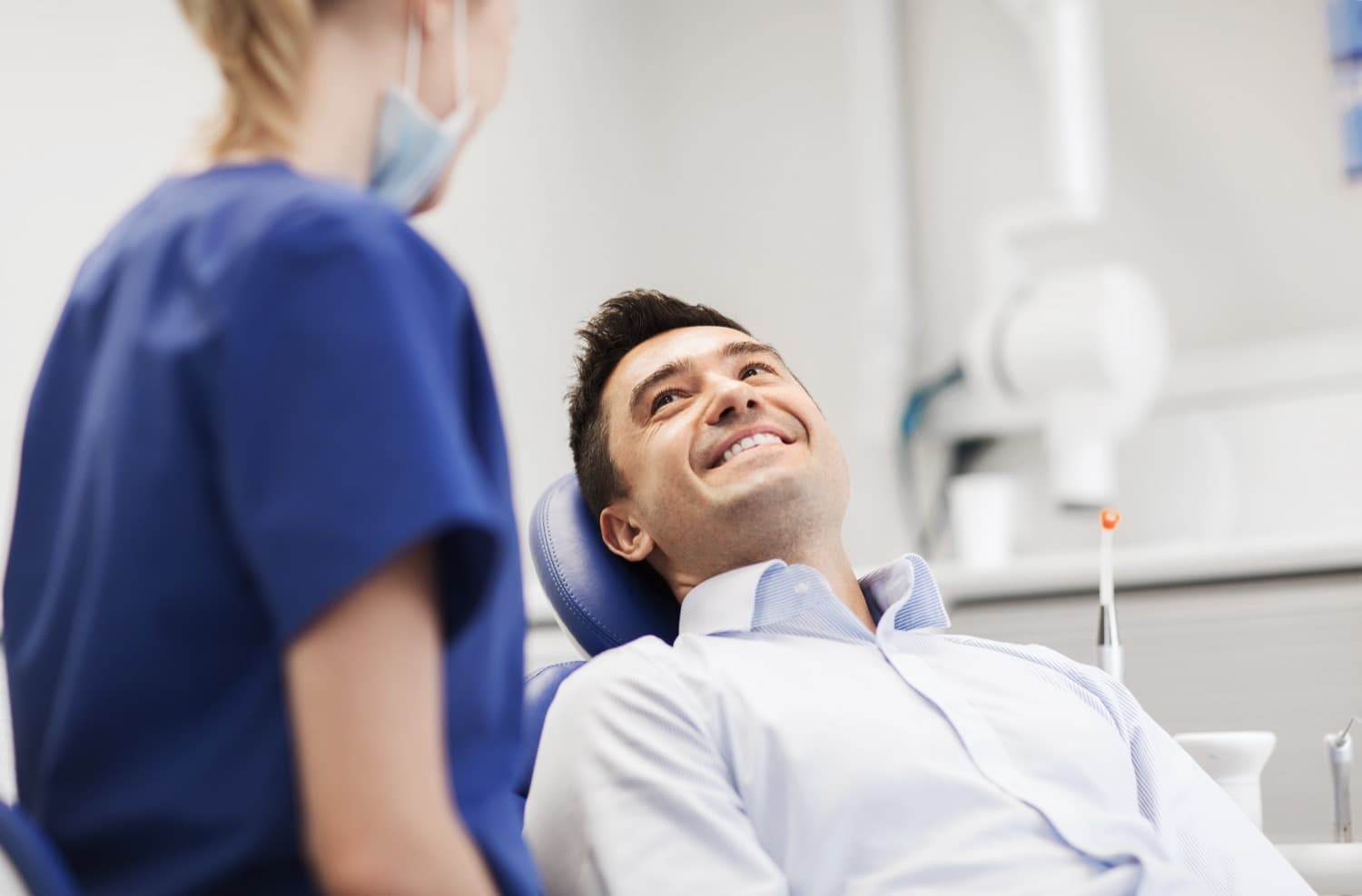 adult man smiling in dentist chair as he speaks with his hygienist and doctor about inlays and onlays